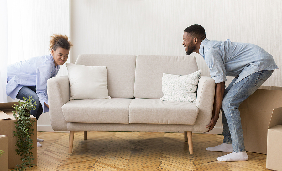 A young couple tries to lift a white couch during their move.