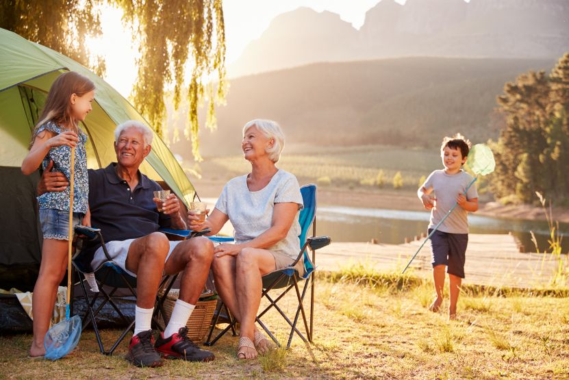 A senior couple enjoys camping with their grandchildren near a lake.