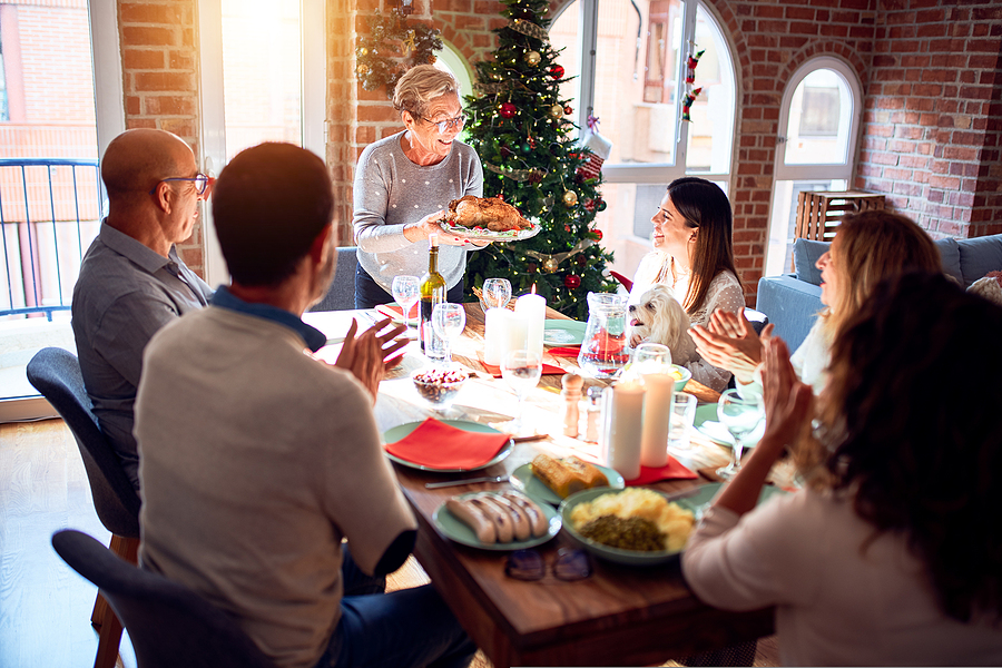 A multi-generational group of friends enjoys a meal surrounded by winter holiday decorations.
